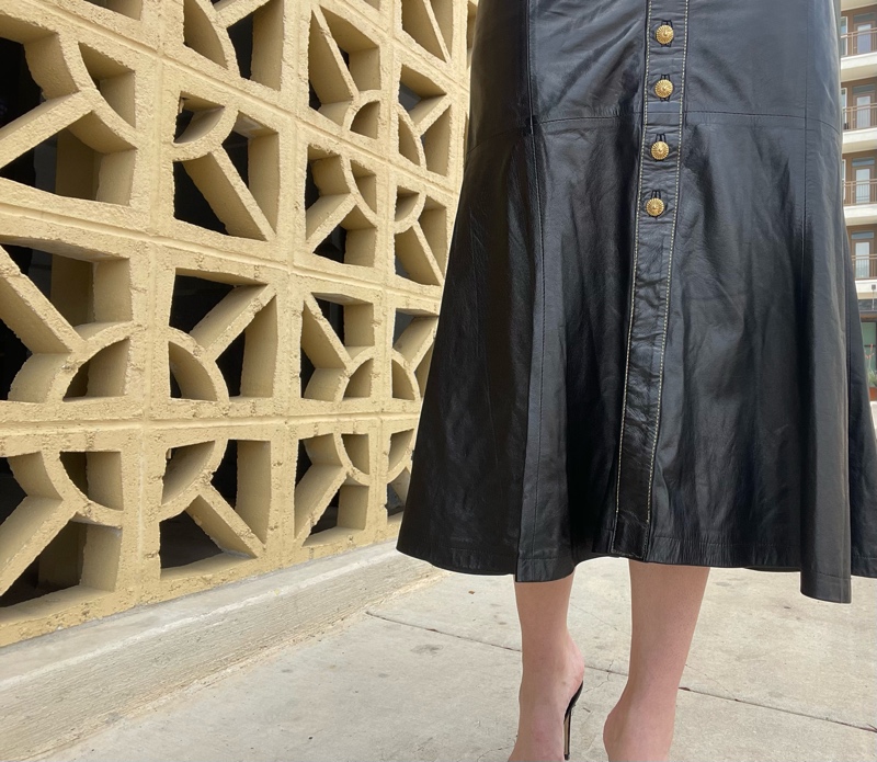 a woman in a Roberto Cavalli leather skirt with gold buttons, a white tee shirts and black sandal pumps