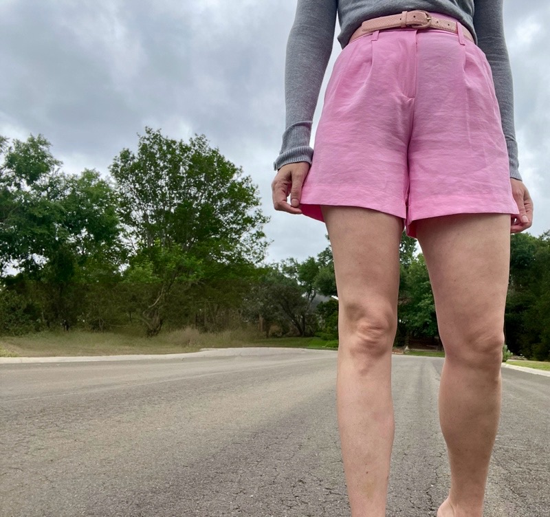 a woman in pink linen shorts, a grey sweater and leopard mules 