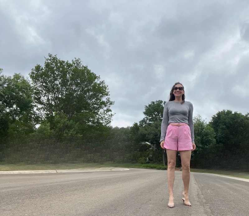 a woman in pink linen shorts and a grey sweater and leopard mules
