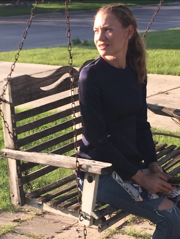 a woman in a navy peplum top and distressed jeans with metallic heels and a painted clutch