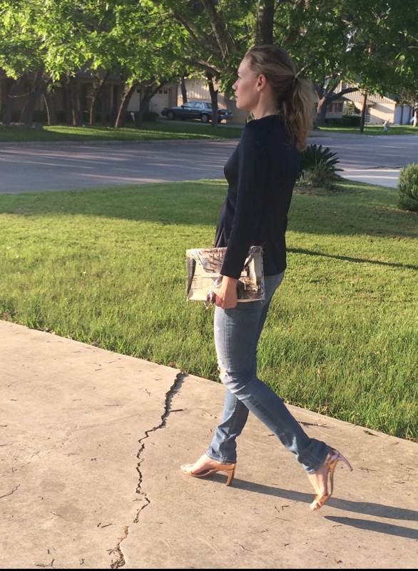 a woman in a navy peplum top and distressed jeans with metallic heels and a painted clutch