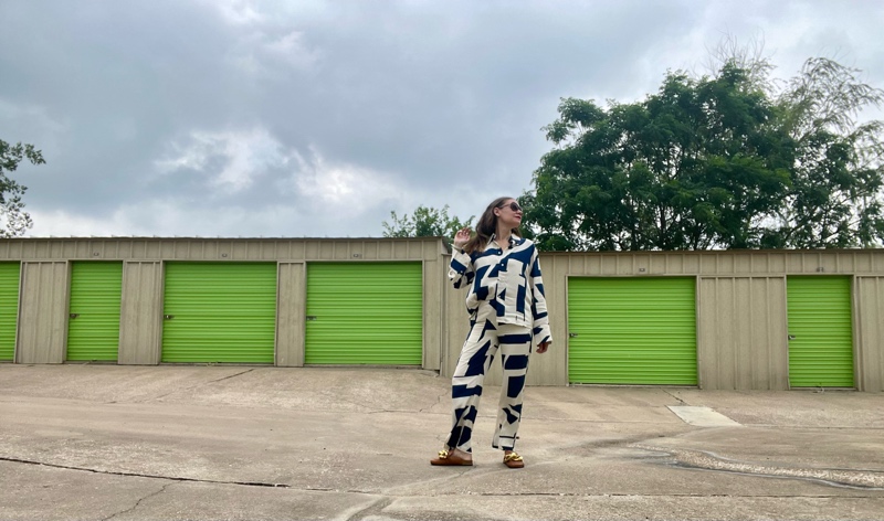 a woman in a blue and white linen pant and Long sleeve set in front of green doors and concrete