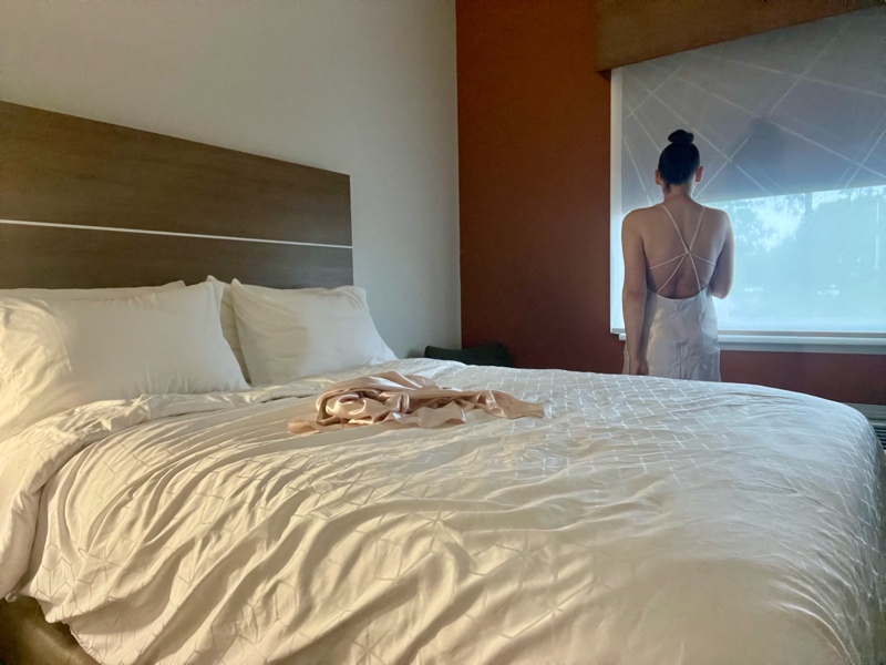 a woman in a pink peignoir set by a wind with a white bed