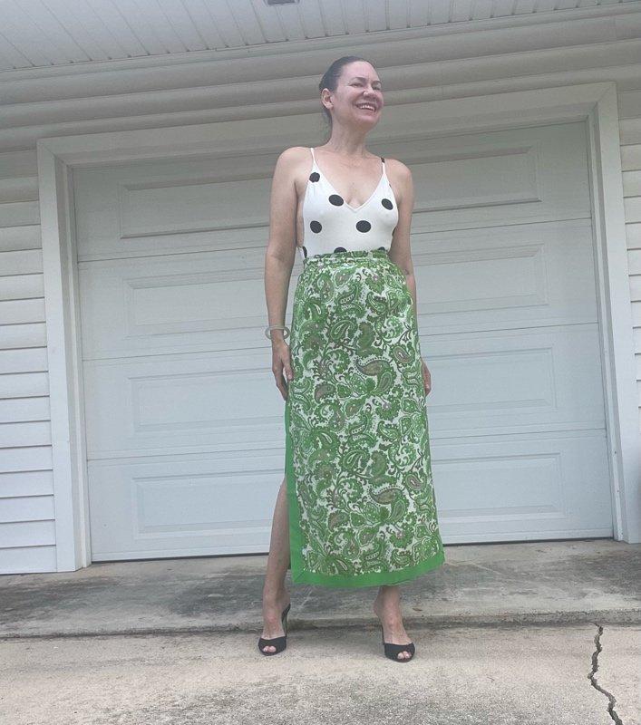 a woman in a white with black polka dot s body suit and a green with embroidered panels maxi skirt and black heeled mules 