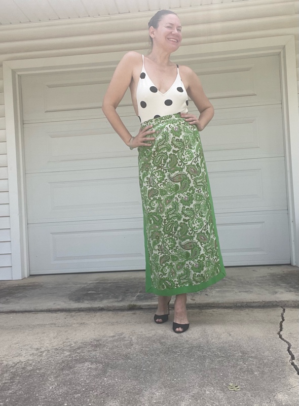 a woman in a white with black polka dot s body suit and a green with embroidered panels maxi skirt and black heeled mules 