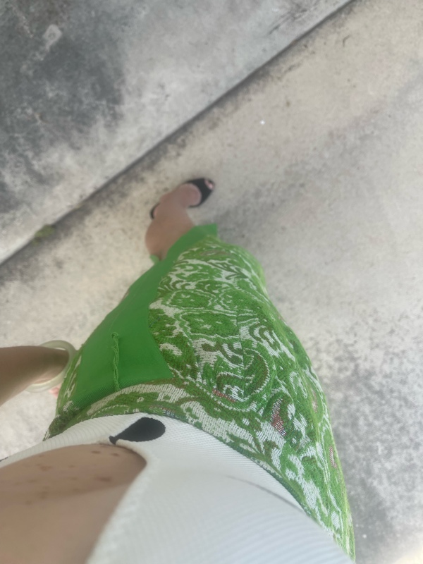 a woman in a white with black  polka dot s body suit  and a green with embroidered panels maxi skirt and black heeled mules 