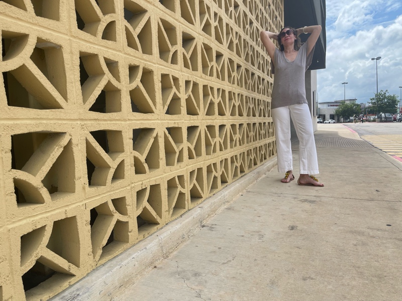 a woman in white jeans and a sweater vest with raffia sandals