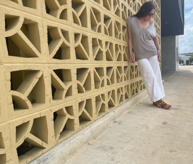 a woman in white jeans and a sweater vest with raffia sandals