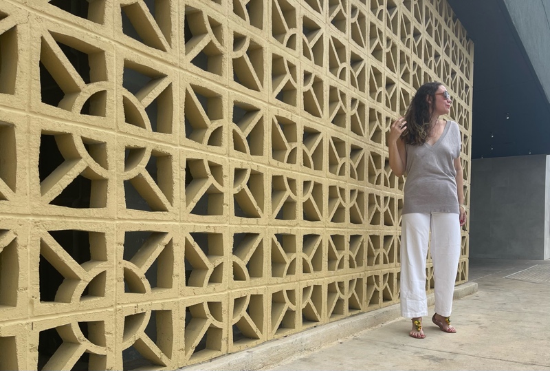 a woman in white jeans and a sweater vest with raffia sandals 