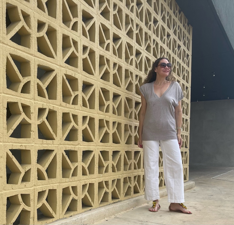 a woman in white jeans and a sweater vest with raffia sandlas