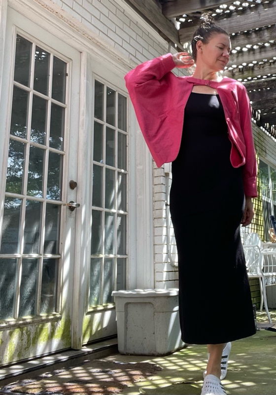 a woman in a black maxi dress with a pink bolero and white and black clogs