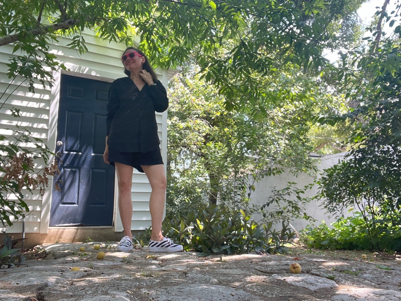 a woman in black linen shorts and button down with black and white sneakers 
