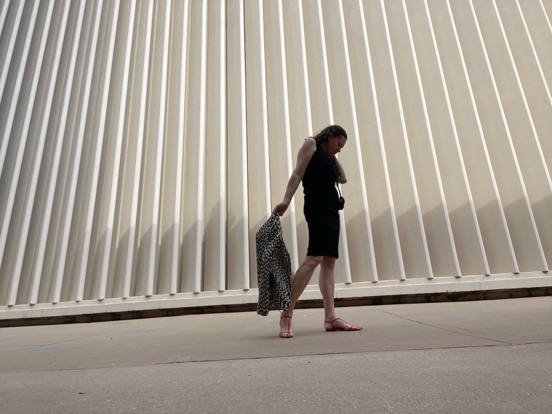 a woman in a polka dot jacket, sweater vest, pencil skirt, wallet, and red sandals 